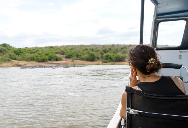 Woman watches wildlife and hippos while on a boat cruise safari at Kazinga Channel - Queen Elizabeth National Park